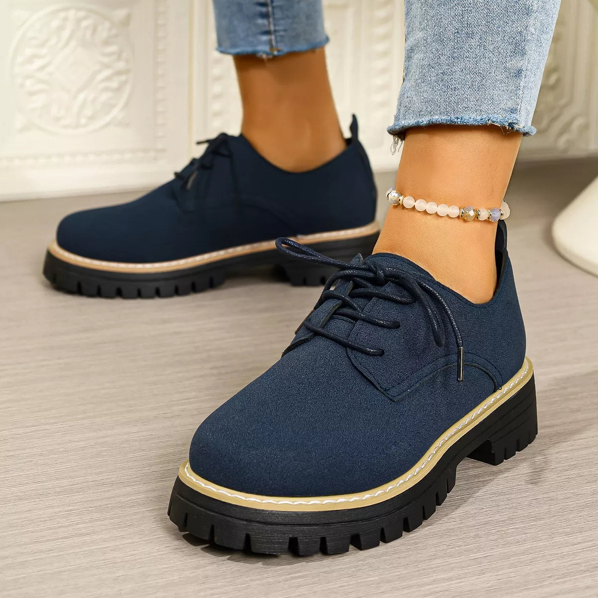 Navy blue shoes with thick soles worn by a person on a neutral background