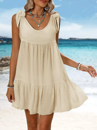 Woman wearing a beige dress on a beach with clear blue water and sky.