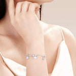 Silver bracelet with charms on a person's wrist against a neutral background