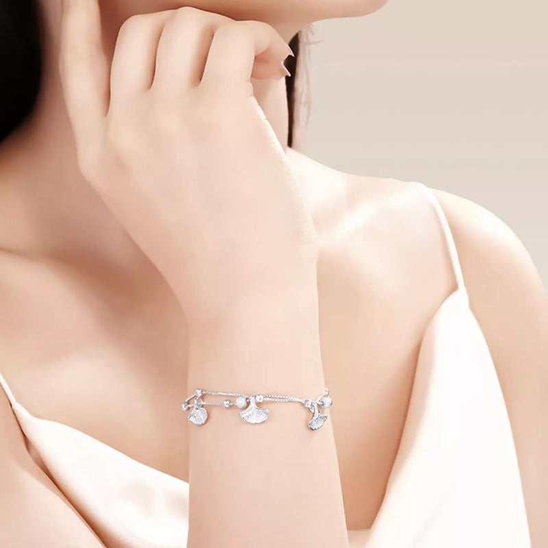 Silver bracelet with charms on a person's wrist against a neutral background
