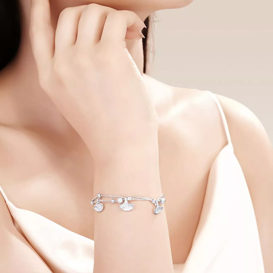 Silver bracelet with charms on a person's wrist against a neutral background