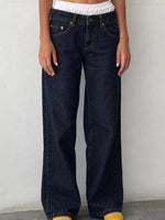 A person wearing dark indigo wide-leg jeans with a white cropped top and yellow shoes, standing against a plain light gray wall.