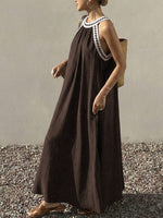 Woman wearing a brown dress with white lace details, standing on a gravel surface.