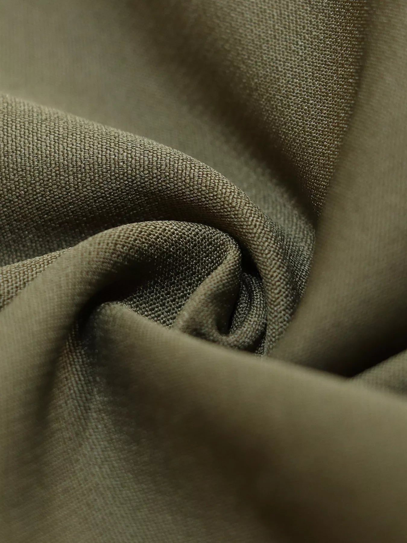 A close-up of draped olive green fabric with a fine woven texture, showing soft folds and shadows.