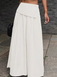 Person wearing a long white skirt standing on a sidewalk.