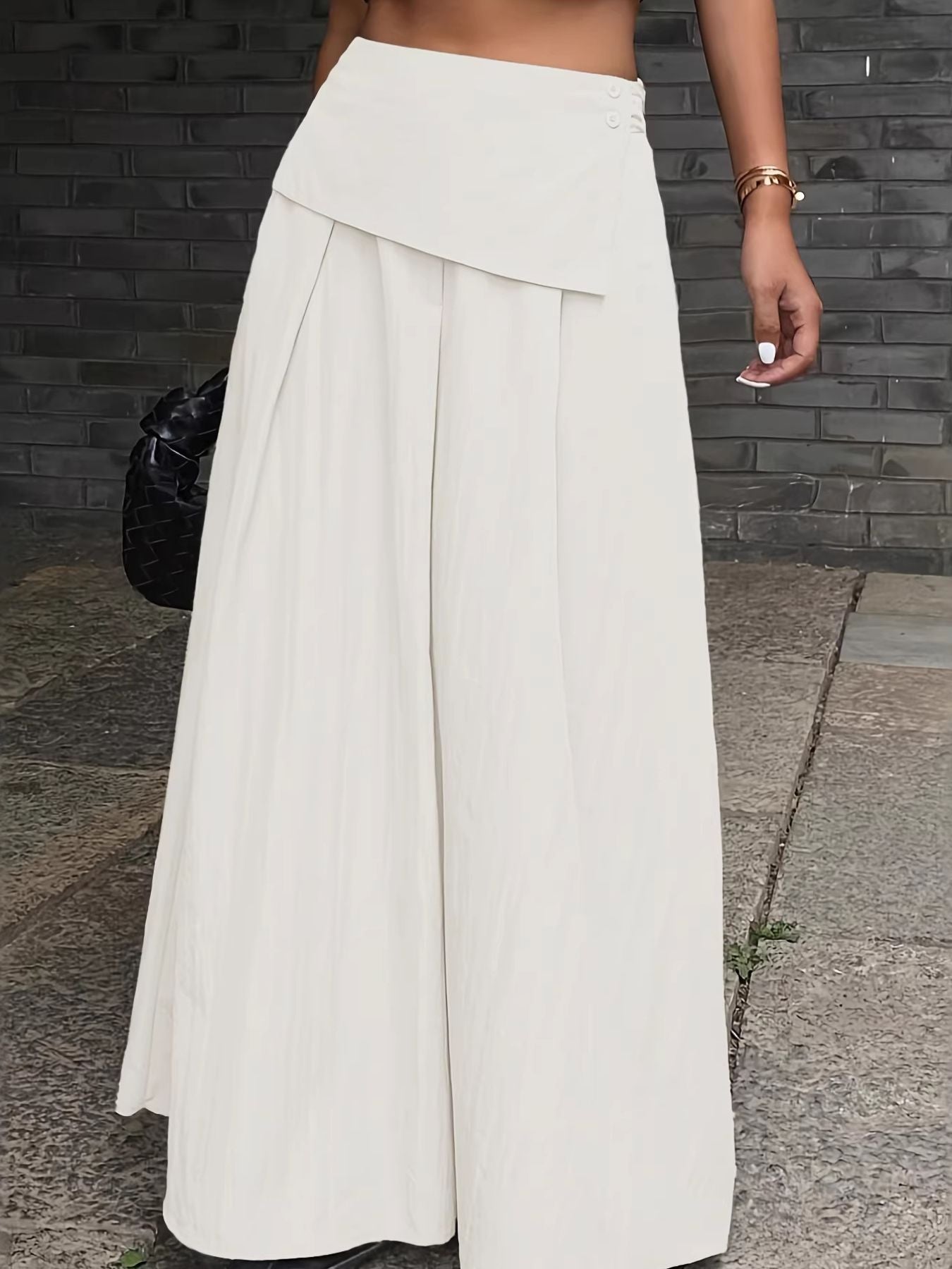 Person wearing a long white skirt standing on a sidewalk.