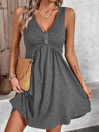 Woman wearing a gray sleeveless dress holding a beige clutch against a neutral background
