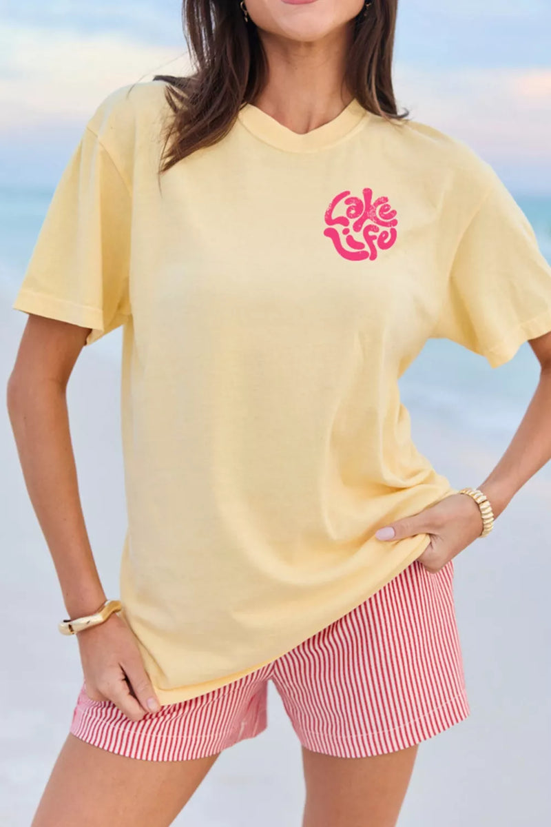 Woman wearing a yellow t-shirt with a pink logo and red and white striped shorts against a blue sky.