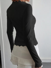 Person wearing a black long-sleeve top and white pleated skirt against a plain background