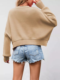 Person wearing a beige sweater and denim shorts on a plain background