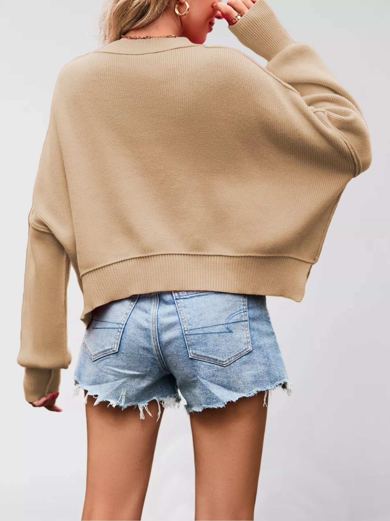 Person wearing a beige sweater and denim shorts on a plain background