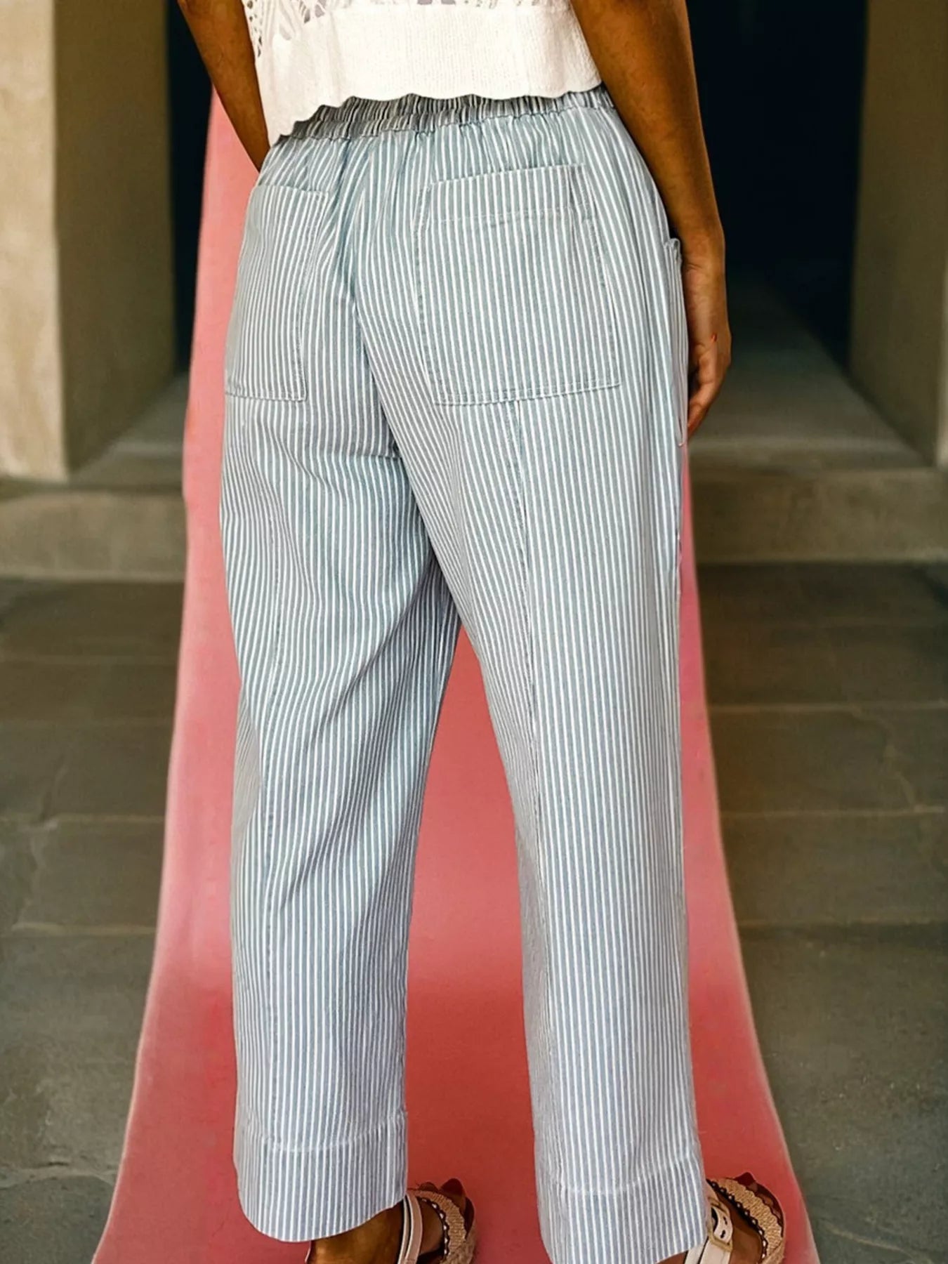 Person wearing light blue striped pants on a red platform with a neutral background