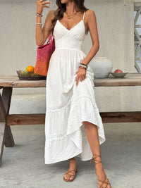 Woman in a white dress standing outdoors near a wooden table with fruit and a vase.