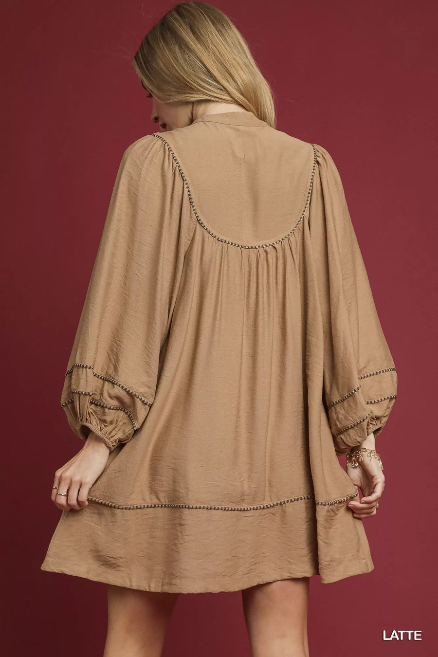 Woman wearing a beige dress with intricate detailing on a red background