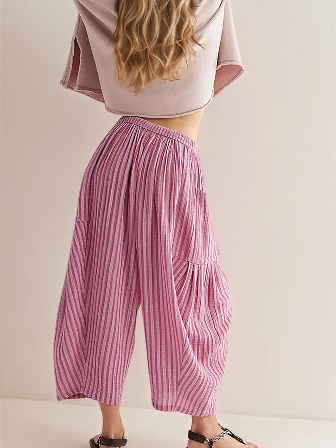 Person wearing a pink crop top and striped pants on a plain background