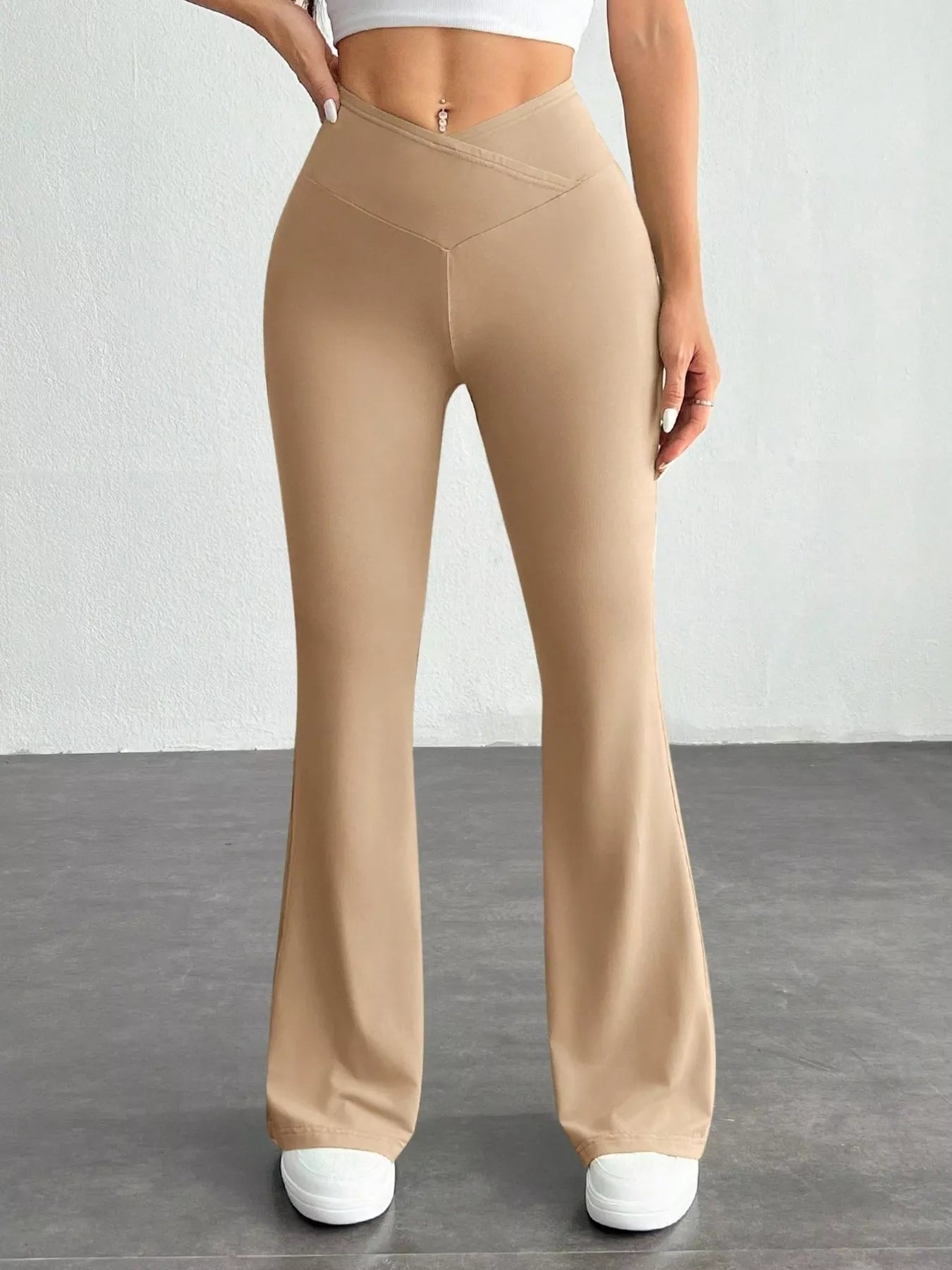 Beige flared pants worn by a person on a gray floor with white background