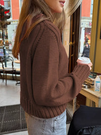 Person wearing a brown sweater holding a coffee cup in an indoor setting.