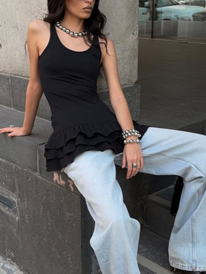 Person wearing a black sleeveless top and light blue jeans sitting on a stone ledge.
