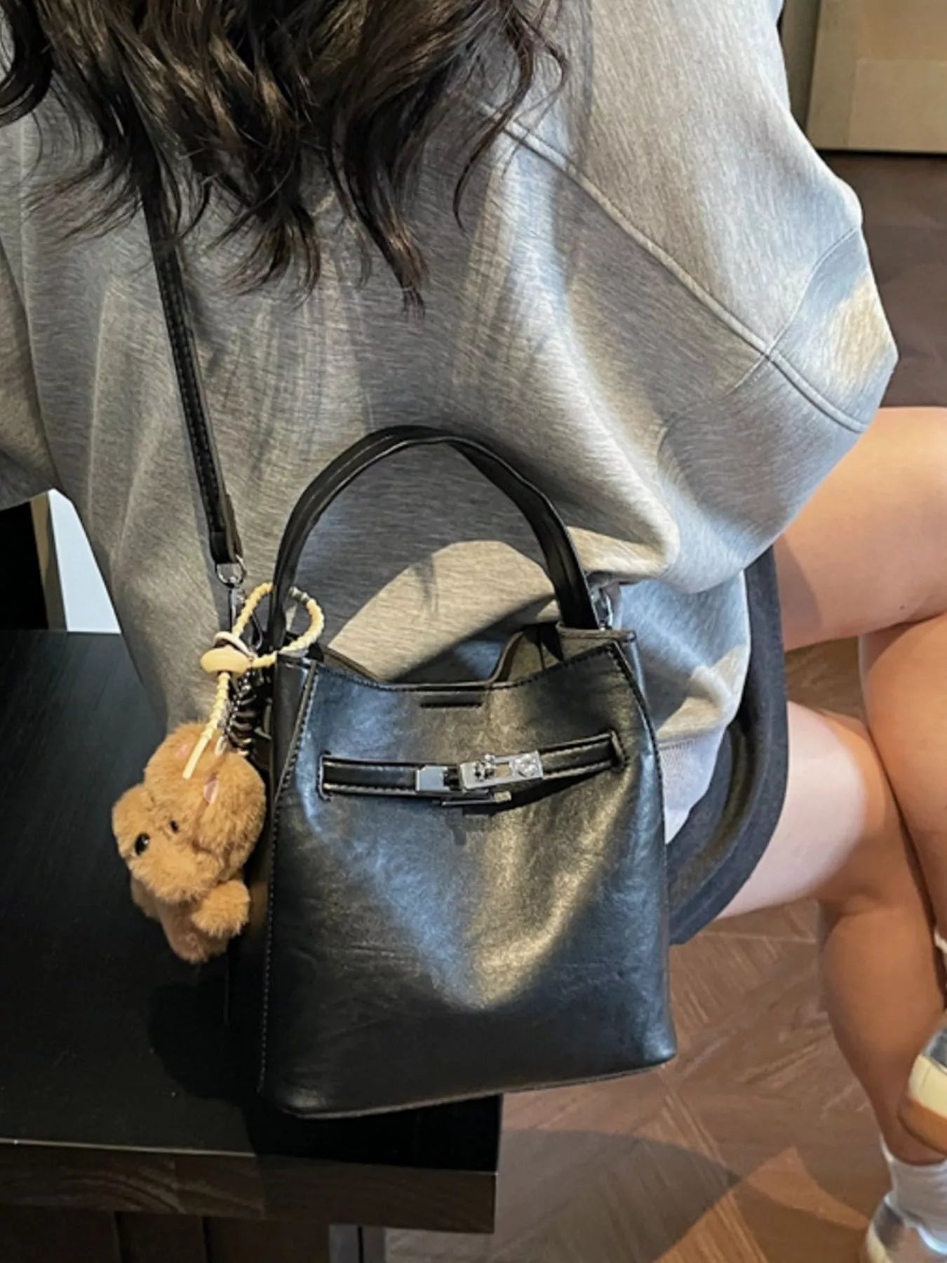 Person holding a black leather handbag with a teddy bear keychain.