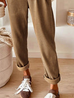 Person wearing brown corduroy pants and brown shoes with white laces on a wooden floor.