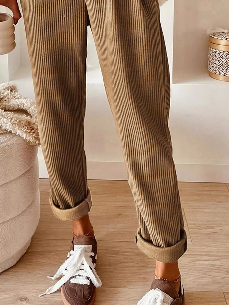 Person wearing brown corduroy pants and brown shoes with white laces on a wooden floor.