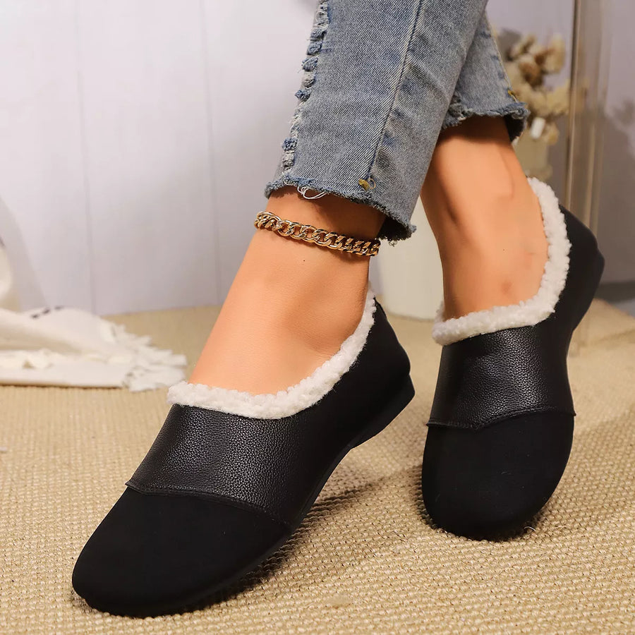Black slip-on shoes with white trim worn by a person on a textured surface.