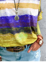 Person wearing a colorful striped shirt with a necklace and denim jeans on a concrete surface.