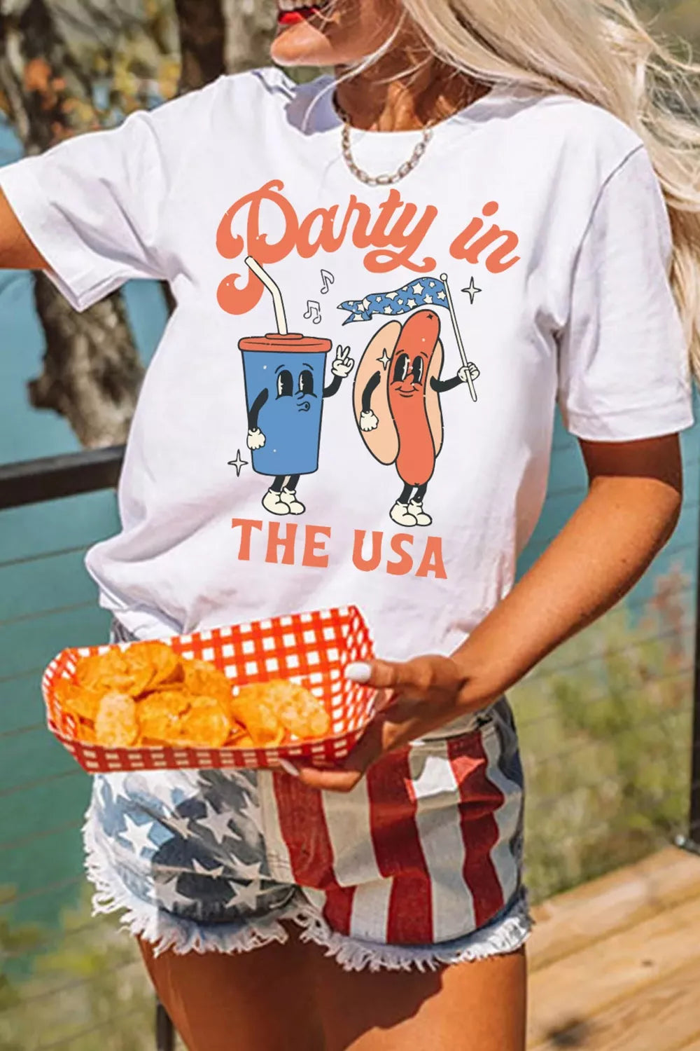 Person wearing a white t-shirt with a colorful graphic and text, holding food outdoors.