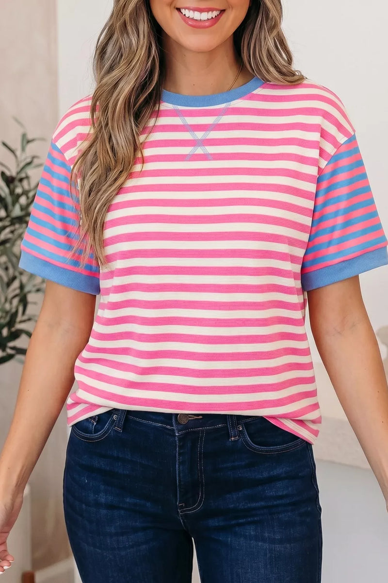 Woman wearing a pink and blue striped shirt with a logo, standing indoors.