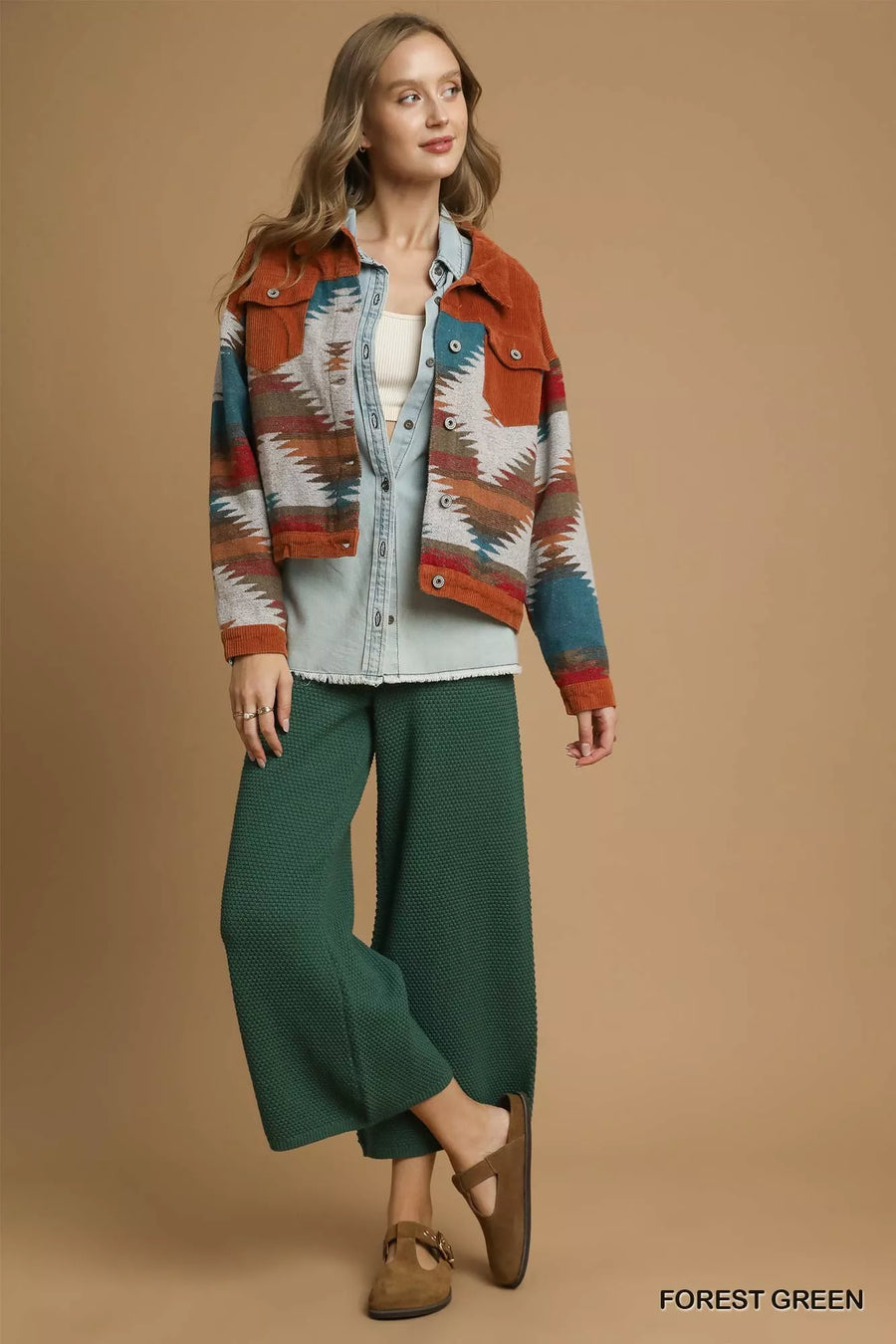 Woman wearing a patterned jacket and green pants on a beige background