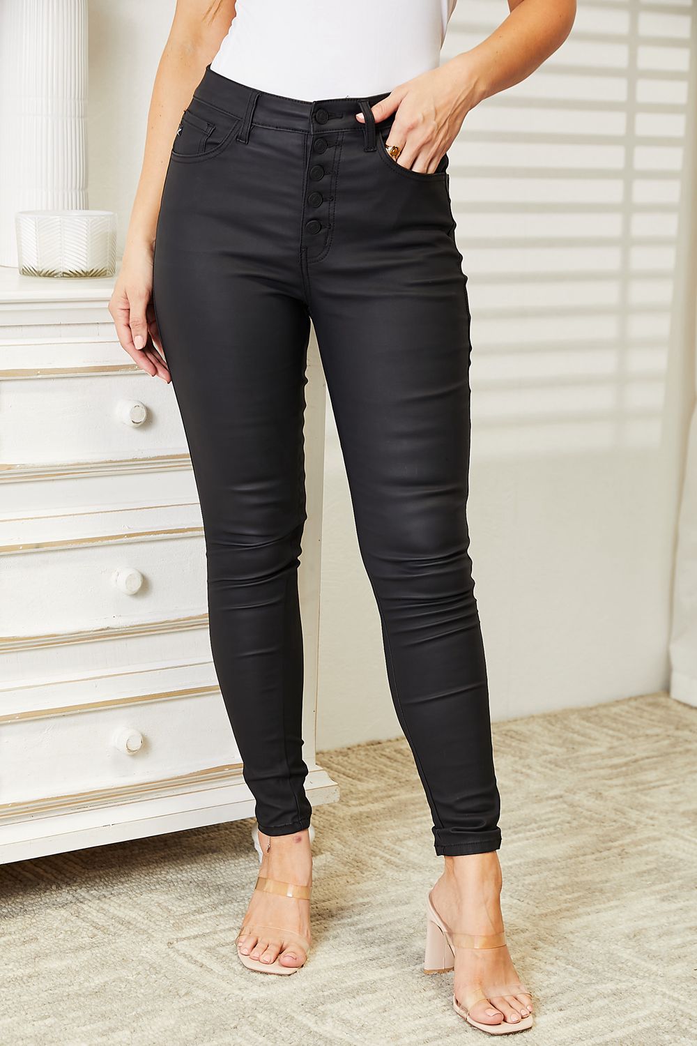 Person wearing black leather pants in a room with a white dresser.