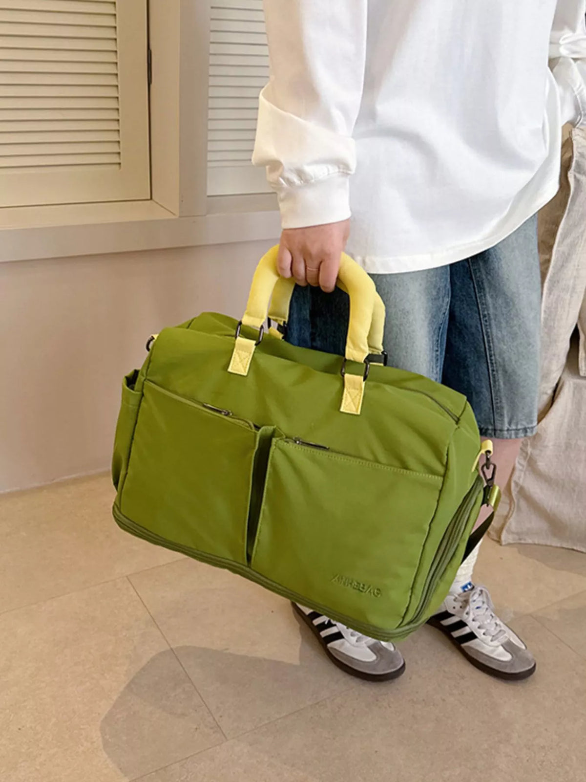 Person holding a green duffel bag with yellow handles indoors.
