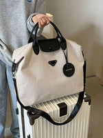Person holding a beige handbag with black handles and accents, standing next to a white suitcase.
