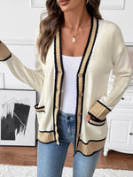 Woman wearing a cream cardigan with black trim in a room setting.