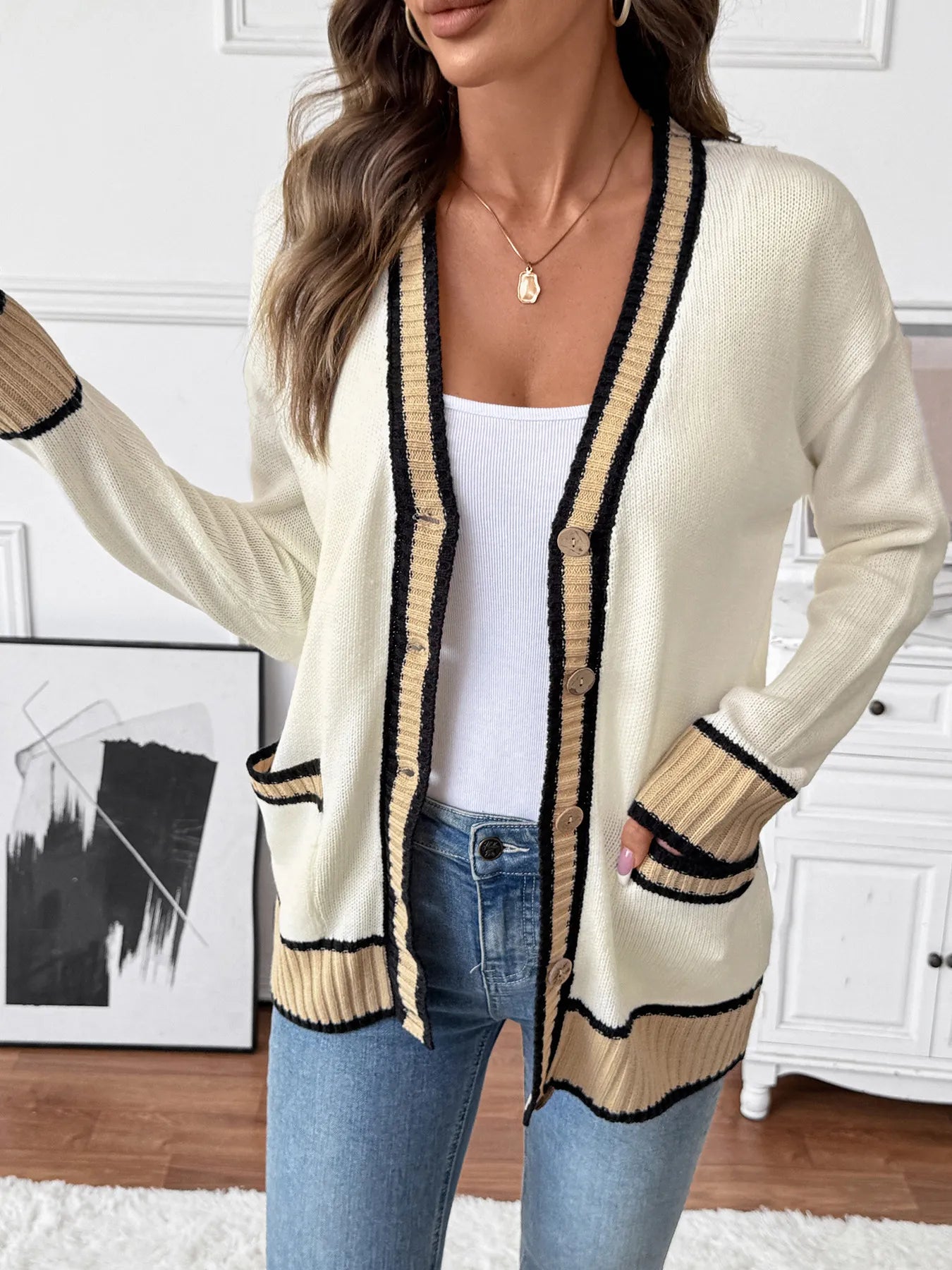 Woman wearing a cream cardigan with black trim in a room setting.