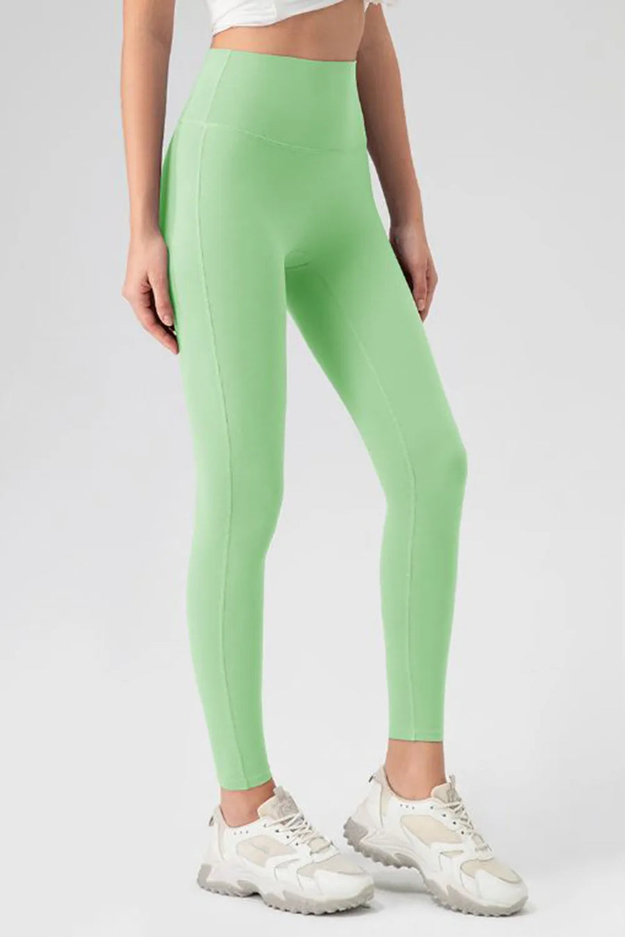 Person wearing green leggings and white sneakers on a plain background