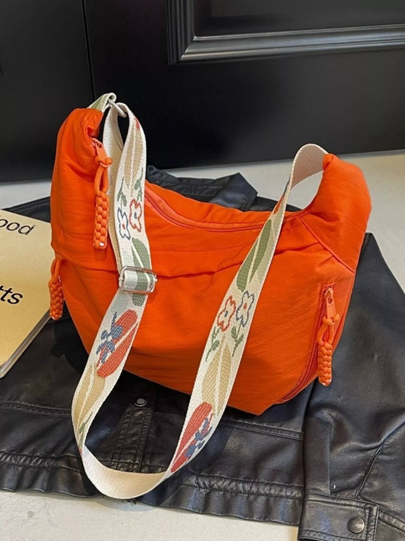 Orange bag with a floral strap on a black leather jacket