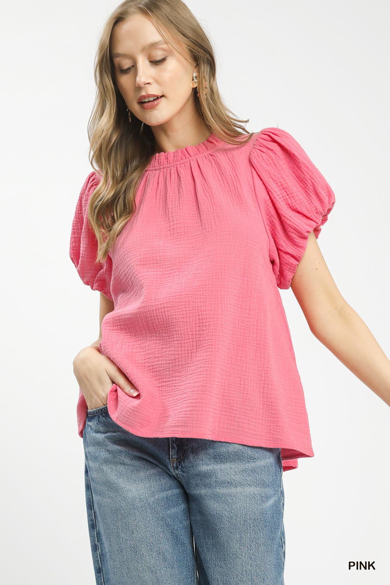 Woman wearing a pink blouse with ruffled sleeves and blue jeans on a white background