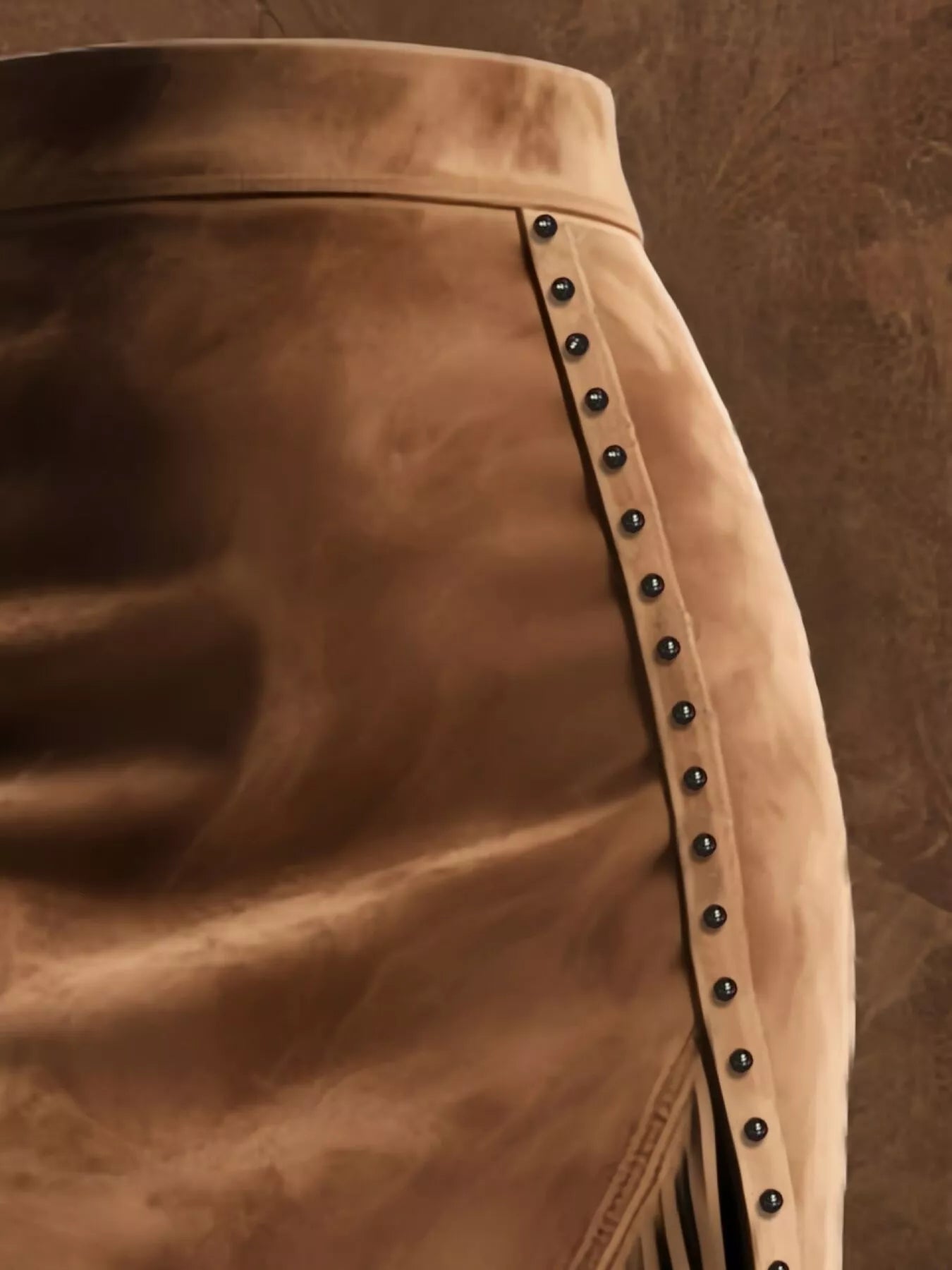 Close-up of a brown leather skirt with studded details on a matching brown background