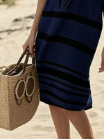 Person wearing a blue and black striped dress holding a straw bag on a beach.