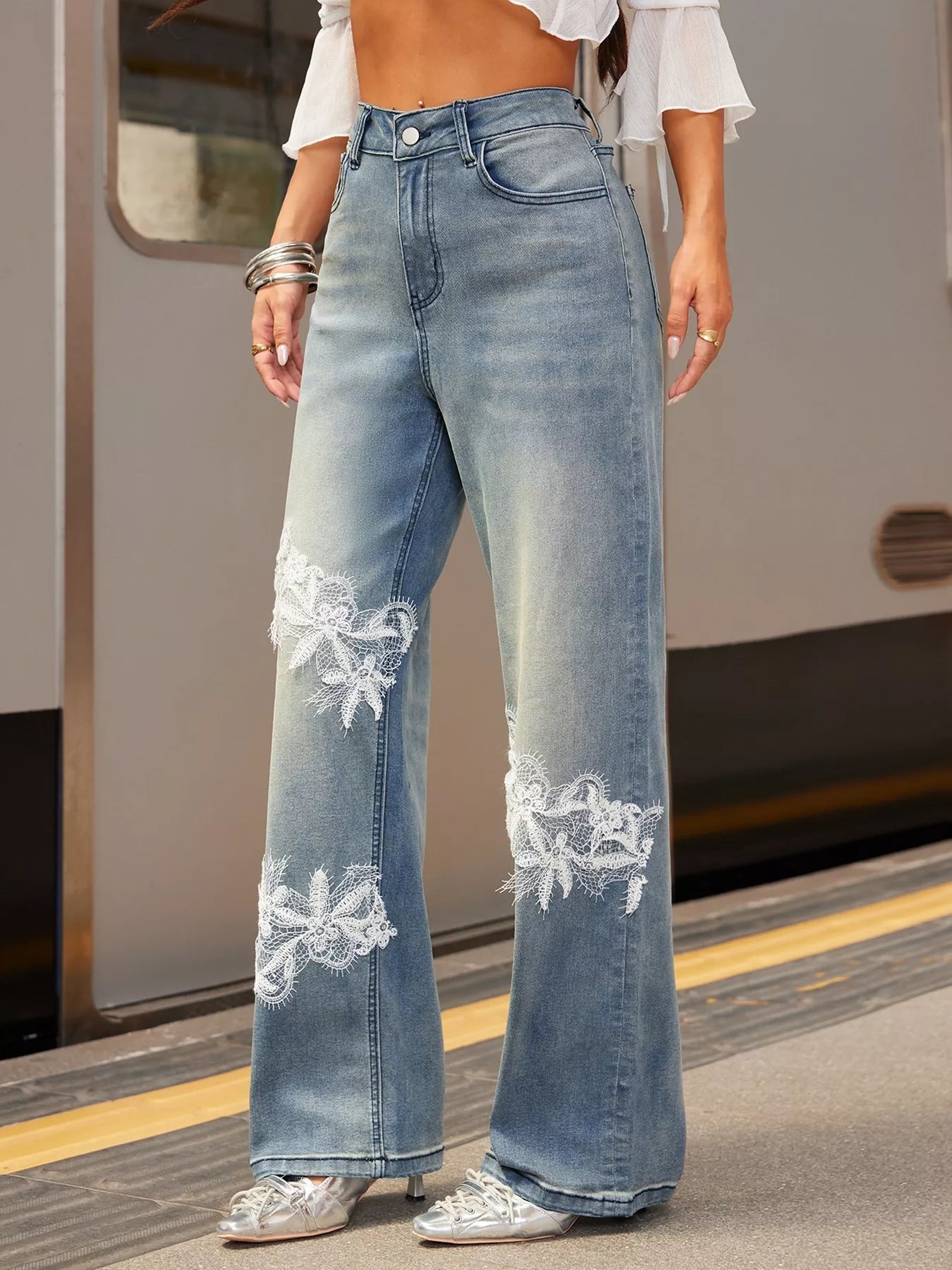 Person wearing light blue jeans with floral embroidery on a train platform.