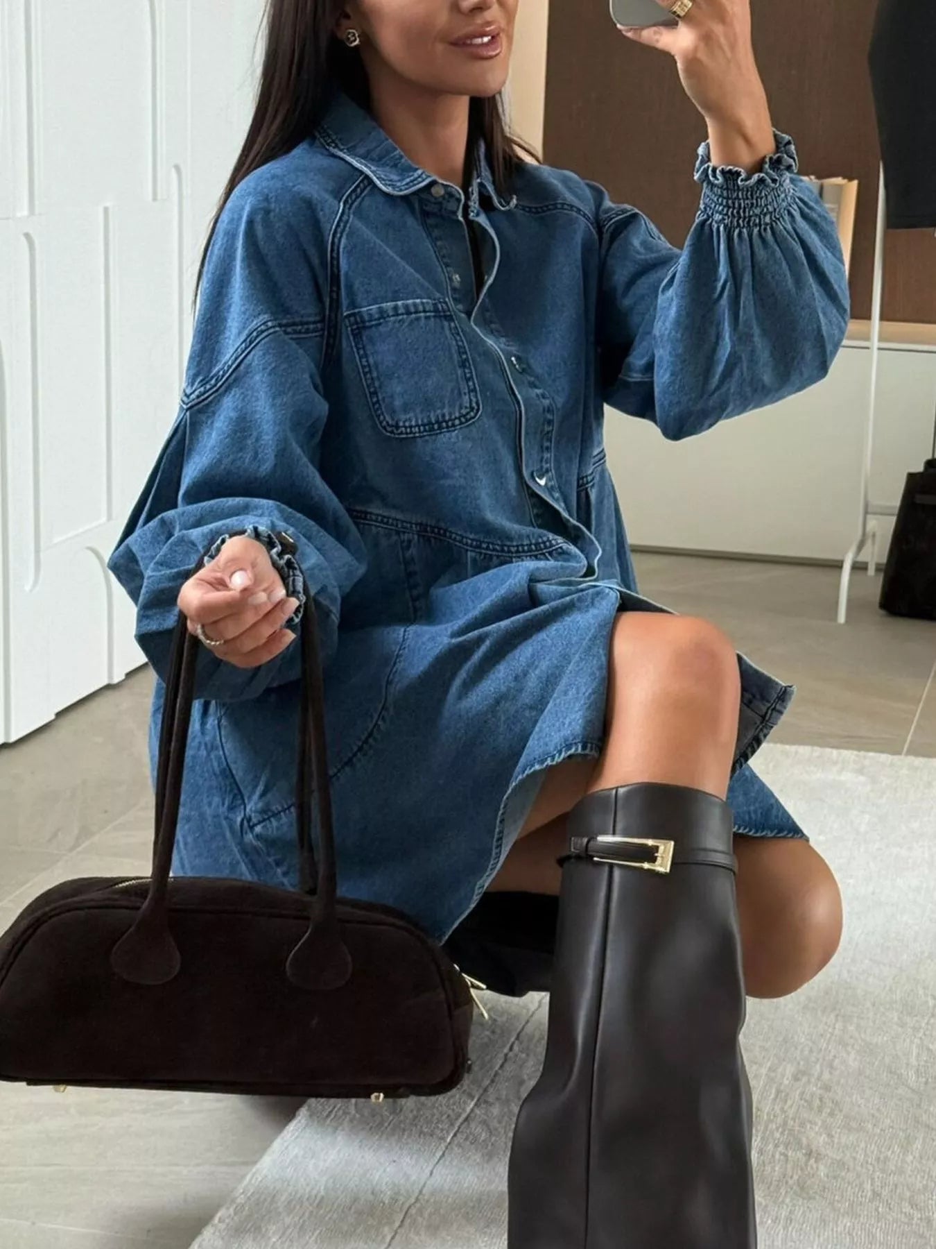 Woman in a denim dress holding a black handbag indoors.