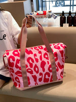 Person holding a pink duffel bag with red leopard print in an indoor setting