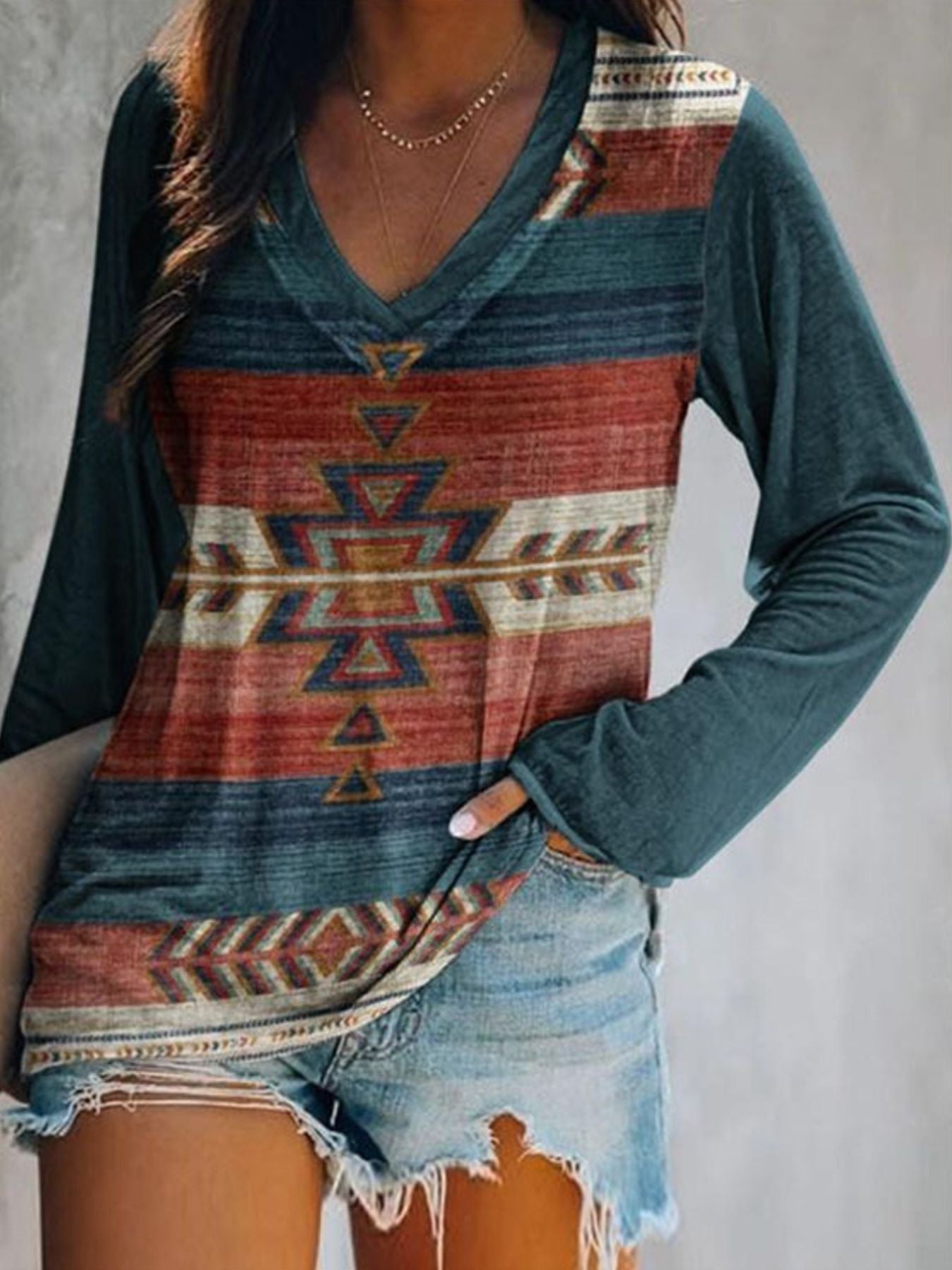 Person wearing a long-sleeve shirt with a geometric pattern and denim shorts against a neutral background