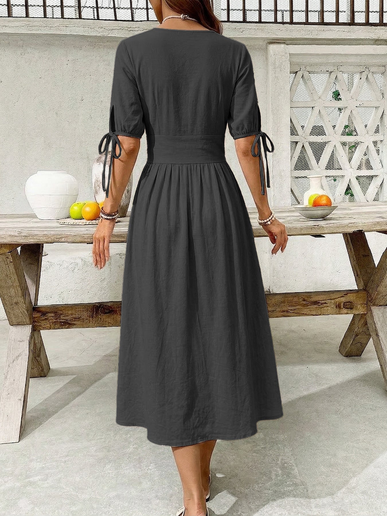 Woman wearing a black dress standing in front of a wooden table with fruit.