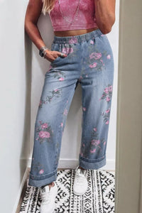 Person wearing floral jeans and a pink top against a white wall.