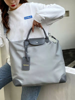 Person holding a gray handbag with a visible brand tag, wearing a white sweatshirt with a logo.