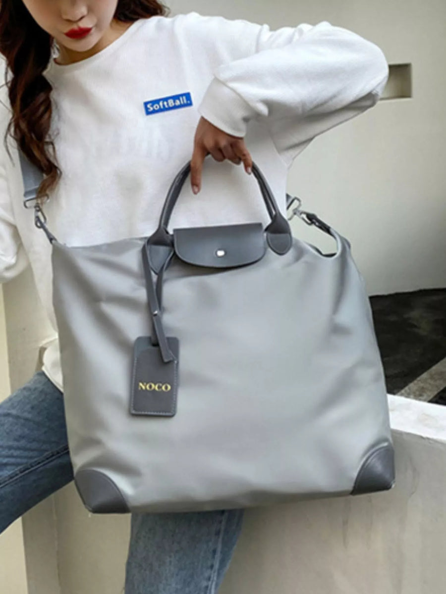 Person holding a gray handbag with a visible brand tag, wearing a white sweatshirt with a logo.