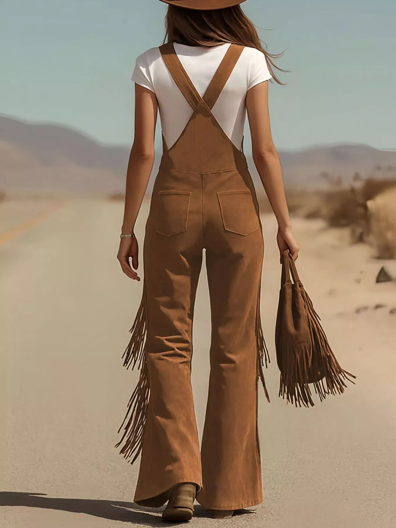 Person wearing brown fringed overalls and white top in a desert setting