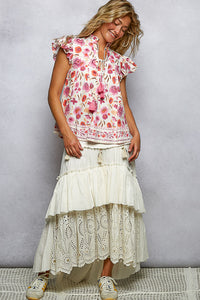 Woman wearing a floral top and white lace skirt against a plain background